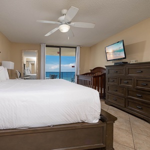 Elegantly decorated master bedroom featuring a king bed, dresser, TV, and a balcony with a view of the beach