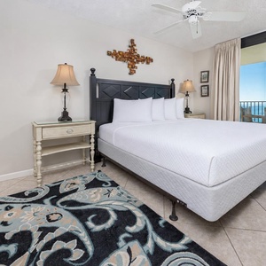 Cozy master bedroom features a king bed, decorative accents, and a sliding door leading to a balcony with a beach view
