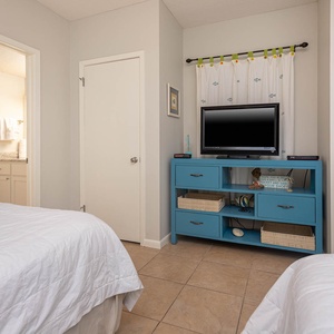 Brightly decorated guest bedroom features two queen beds, a blue media console with a TV, and an en-suite bathroom