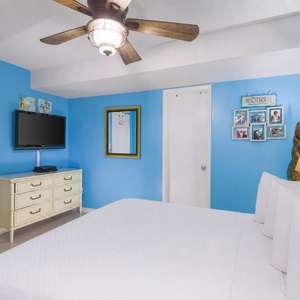 The bedroom features vibrant blue walls, a cozy king bed, a flat-screen TV, and charming beach-themed decor