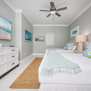 Relax in this inviting guest bedroom featuring two queen beds, a large TV, and coastal artwork