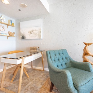 This inviting workspace features a glass-top desk, a cozy blue armchair, and beach-themed décor