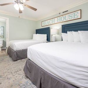 Cozy guest bedroom featuring two double beds with soft linens, a stylish lamp, and a serene beach-themed decor