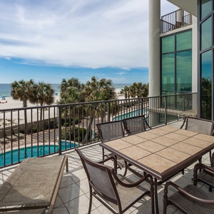 Enjoy the beachfront view from this balcony with a dining table and lounge chairs, perfect for relaxation and meals outdoors