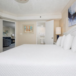 Brightly decorated bedroom features a king bed with plush pillows, leading to a doorway with a view of the living area