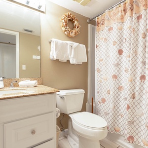 Refreshing guest bathroom featuring a granite countertop, decorative seashell shower curtain, and fresh white towels