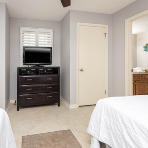 Bright guest bedroom featuring two double beds, a TV on a dresser, and access to a bathroom with decorative fish art