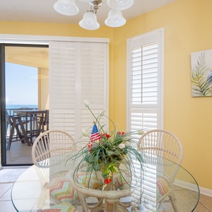 Bright dining area with a glass table and colorful chairs, featuring a stunning view of the beach through sliding doors