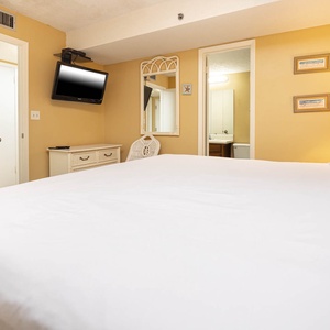 This cozy bedroom features a plush king bed, a mounted TV, and warm yellow walls, creating a relaxing retreat