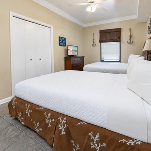 A cozy guest bedroom features two full beds, white linens, a dresser, and beach-themed decor, creating a relaxed atmosphere
