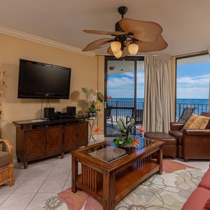 Cozy living area features a large TV, comfortable seating, and a balcony with a view of the tranquil beach