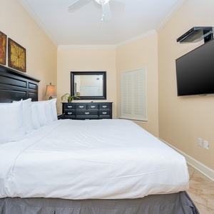 This cozy bedroom features a large king bed, a mounted TV, and decorative artwork, creating a relaxing retreat for guests
