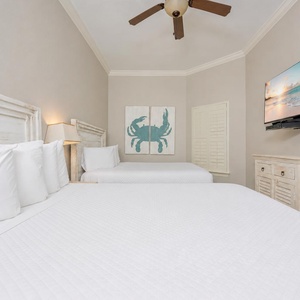 Relaxing guest bedroom featuring two cozy double beds, a TV, and charming coastal decor for a relaxing stay