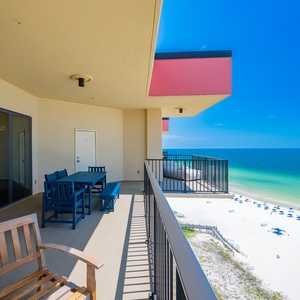 Expansive balcony with blue seating offers breathtaking views of the serene beach and vibrant turquoise waters