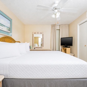 Bright bedroom featuring a king bed, plush bedding, TV, and a dresser, creating a relaxing atmosphere