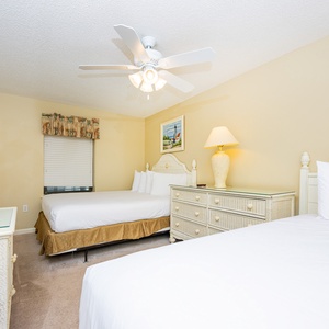 Guest bedroom featuring two queen beds, a dresser, and a ceiling fan, complemented by cheerful artwork