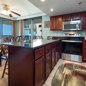 The kitchen features rich wood cabinetry, a dark granite countertop, and a glass dining table with elegant seating