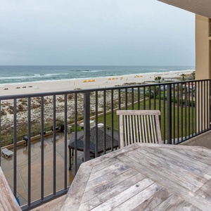A spacious balcony features a wooden table and chairs, offering a serene view of the beach and gentle waves