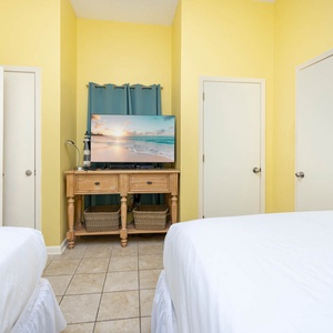 Cozy guest bedroom with two queen beds and a TV on a wooden stand, creating a cheerful and inviting atmosphere