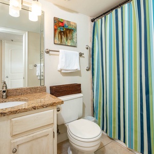 The guest bath features a granite countertop, a striped shower curtain, and a bright, colorful artwork for a refreshing feel