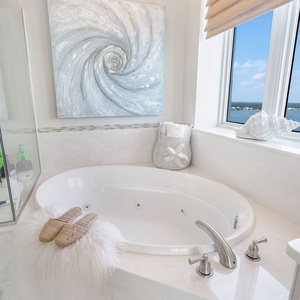 This bathroom features a luxurious jetted tub, a serene coastal artwork, and a lovely view of the water