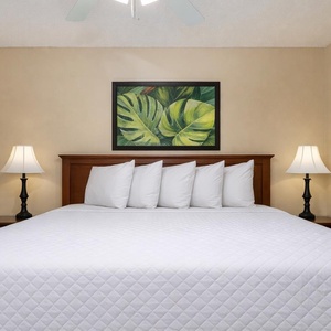 This inviting bedroom features a plush king bed with crisp white linens, complemented by tropical artwork and soft lighting
