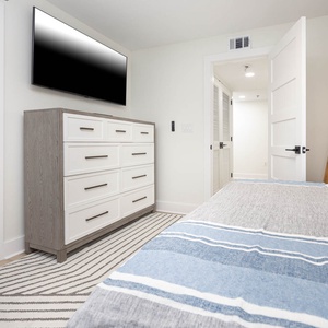 Stylish guest bedroom featuring a queen bed with a striped throw, a built-in twin bunk, dresser, and a wall-mounted TV