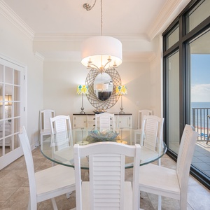 Elegant dining area featuring a glass table, and a beautiful view of the beach from the balcony