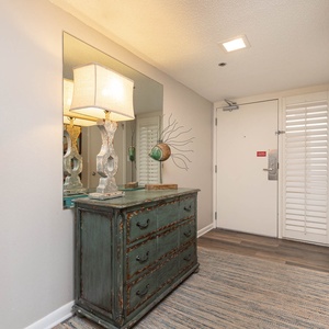 Step into a welcoming entryway featuring a stylish dresser, a decorative lamp, and natural light from the entry door