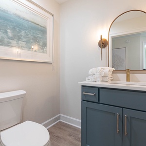 The half bath features a stylish blue vanity, elegant lighting, and serene coastal artwork, perfect for a refreshing retreat