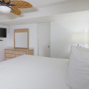 The bedroom features a plush king bed, a wall-mounted TV, a lighted dresser, and beach decor for a relaxed atmosphere