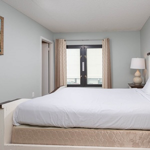 This inviting bedroom features a comfortable bed, soft lighting, and a view through large windows, perfect for relaxation