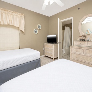 Guest bedroom featuring two twin beds, a TV, and a dresser with a mirror, leading to an en-suite bathroom