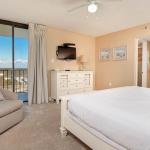 Bright master bedroom featuring a queen bed, a cozy armchair, and a private balcony with expansive views
