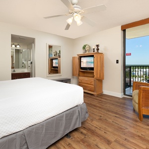 Bright and airy master bedroom features a king bed, wooden furniture, and a cozy chair, leading to the balcony