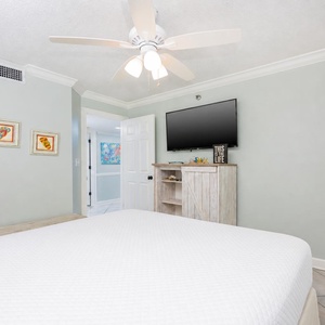 Brightly colored artwork complements the serene green walls in this inviting guest bedroom featuring a queen bed and wall TV