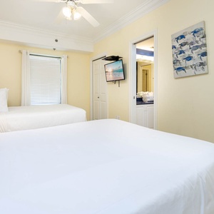 Cozy guest room featuring two double beds, a mounted TV, and easy access to the bathroom with fresh towels