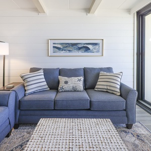 Relax in this inviting living area featuring a cozy sofa, decorative pillows, and a view of the beachfront balcony