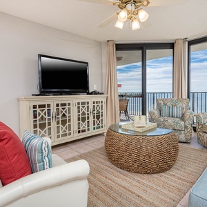 Cozy living area features a light blue sofa with queen sleeper, tropical-patterned chairs, and a view of the gulf
