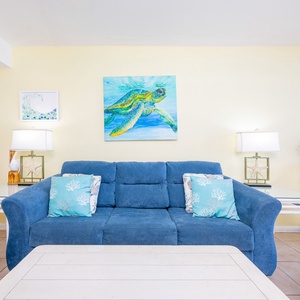 Soft cushions and coastal art invite you to sink into the living room's cozy blue sofa with a queen sleeper