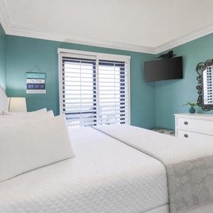 Master bedroom features a plush king bed, decorative accents, and a TV, with natural light streaming from the balcony