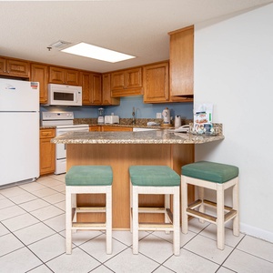 Modern kitchen features light wood cabinetry, granite countertops, and a breakfast bar with three stools for casual dining