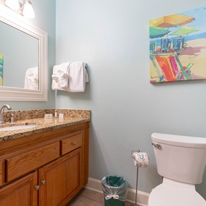 Brightly colored artwork complements the granite countertop and wooden cabinetry in this inviting guest bathroom space