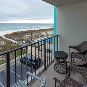 Enjoy a relaxing moment on the balcony with comfortable seating and a scenic view of the pristine beach and azure waters