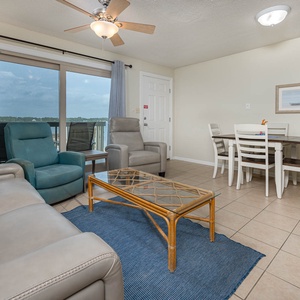 The living area features a seating arrangement, a glass coffee table, and a lovely lagoon view through large sliding doors