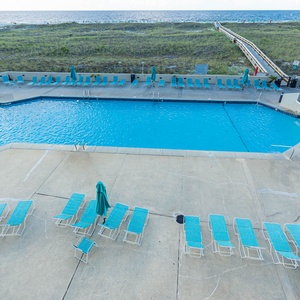 Pool area features turquoise lounge chairs and a clear blue pool, with a scenic view of the beach in the background