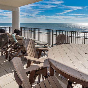 This expansive balcony features panoramic views, comfortable seating, and a dining table overlooking the pool and beach
