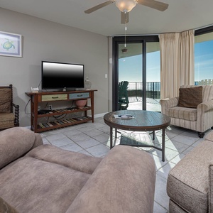 Cozy living area features a flat-screen TV, comfortable seating, and access to a balcony with a stunning beachfront view