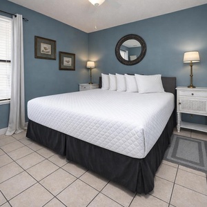 This cozy bedroom features a large bed with crisp white linens, a stylish lamp, and charming artwork on soft blue walls
