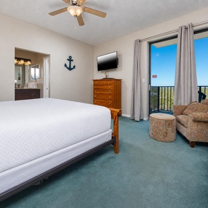 Bright master bedroom featuring a king bed, cozy seating area, and a balcony with a view, adorned with nautical decor